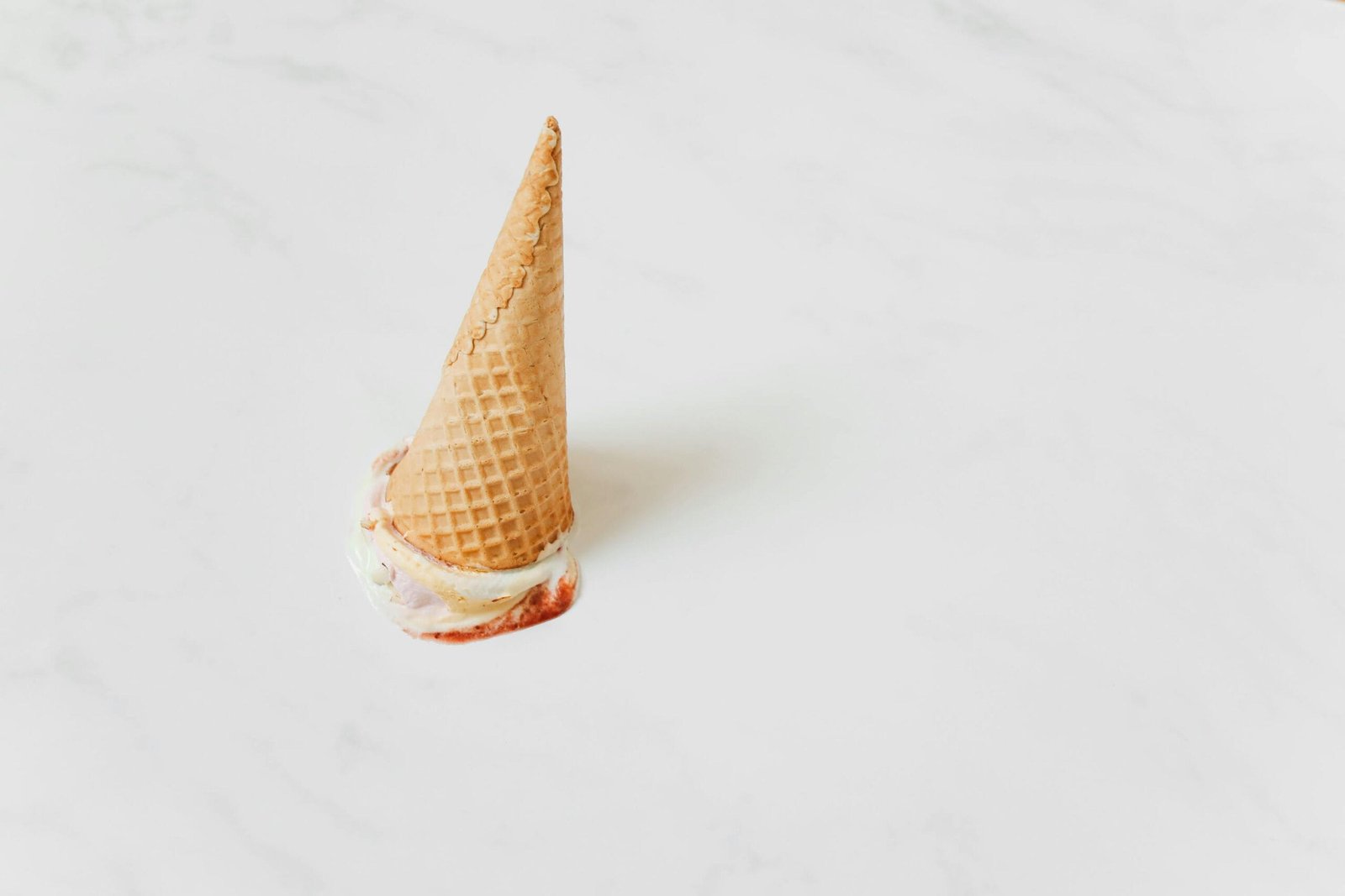 An upside-down ice cream cone melting on a white marble surface.